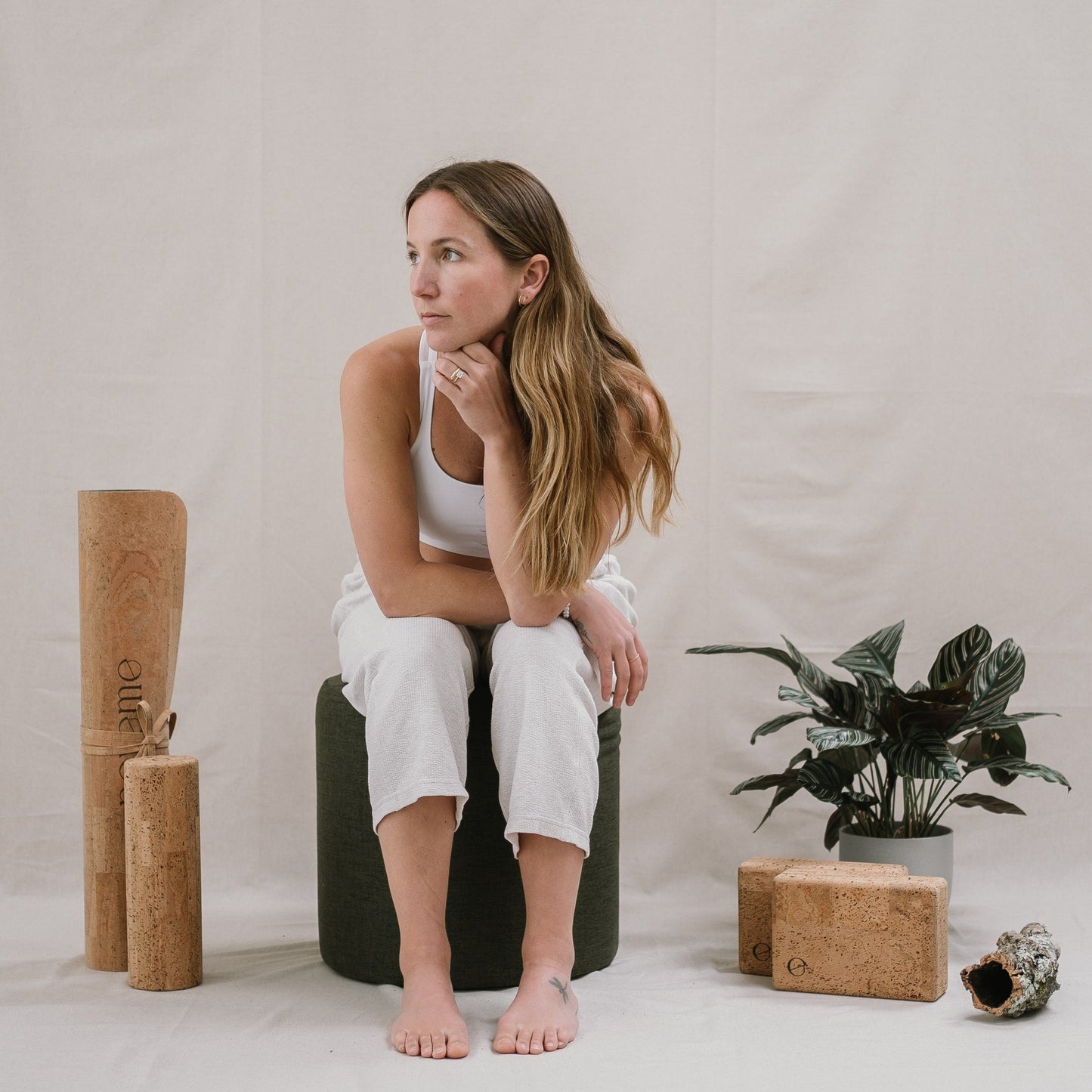 Woman seated next to a Noveme complete yoga set, which includes a cork yoga mat, two yoga blocks and a roller