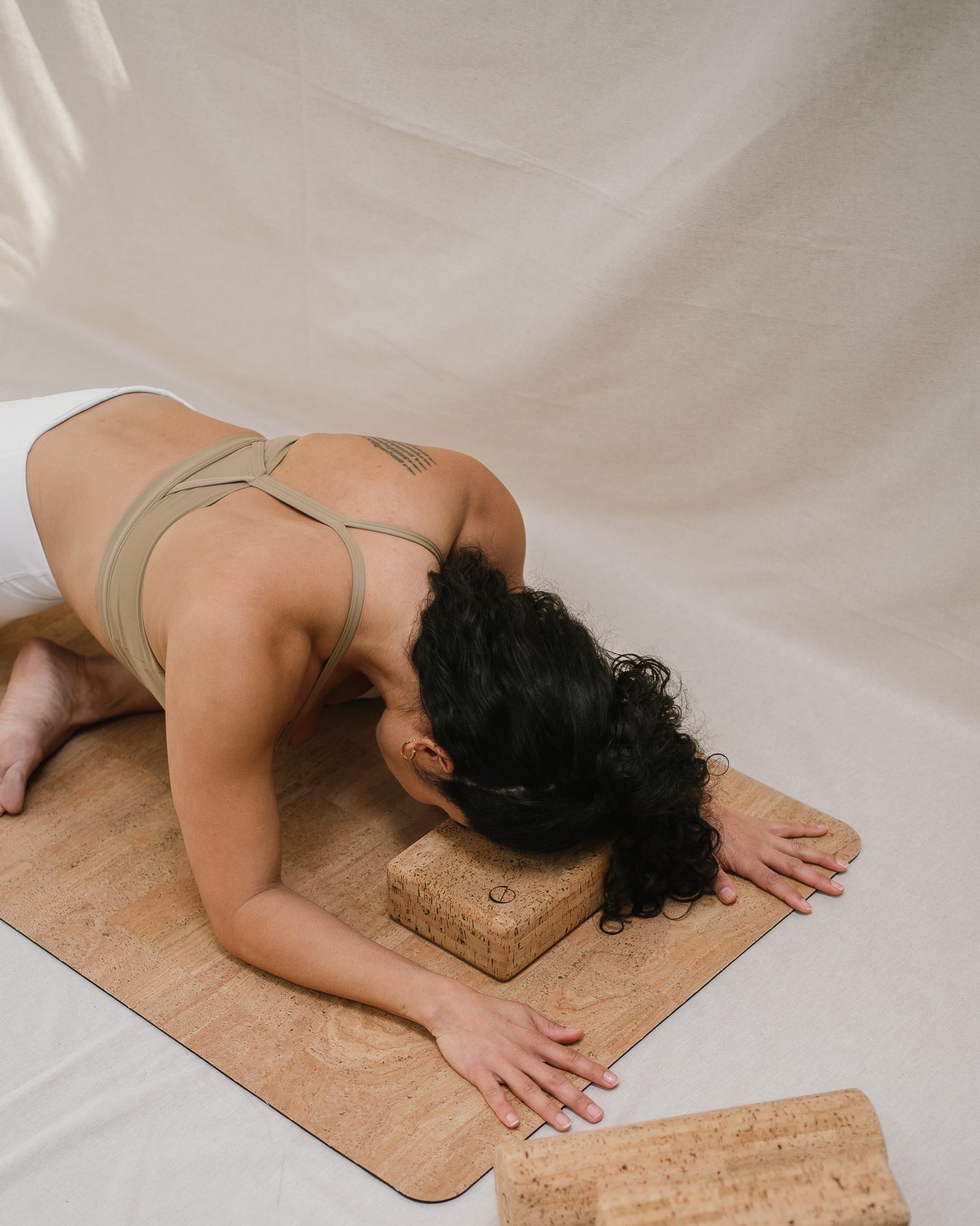 Yogi doing pigeon pose on a cork yoga mat with her head supported by a Noveme cork yoga block