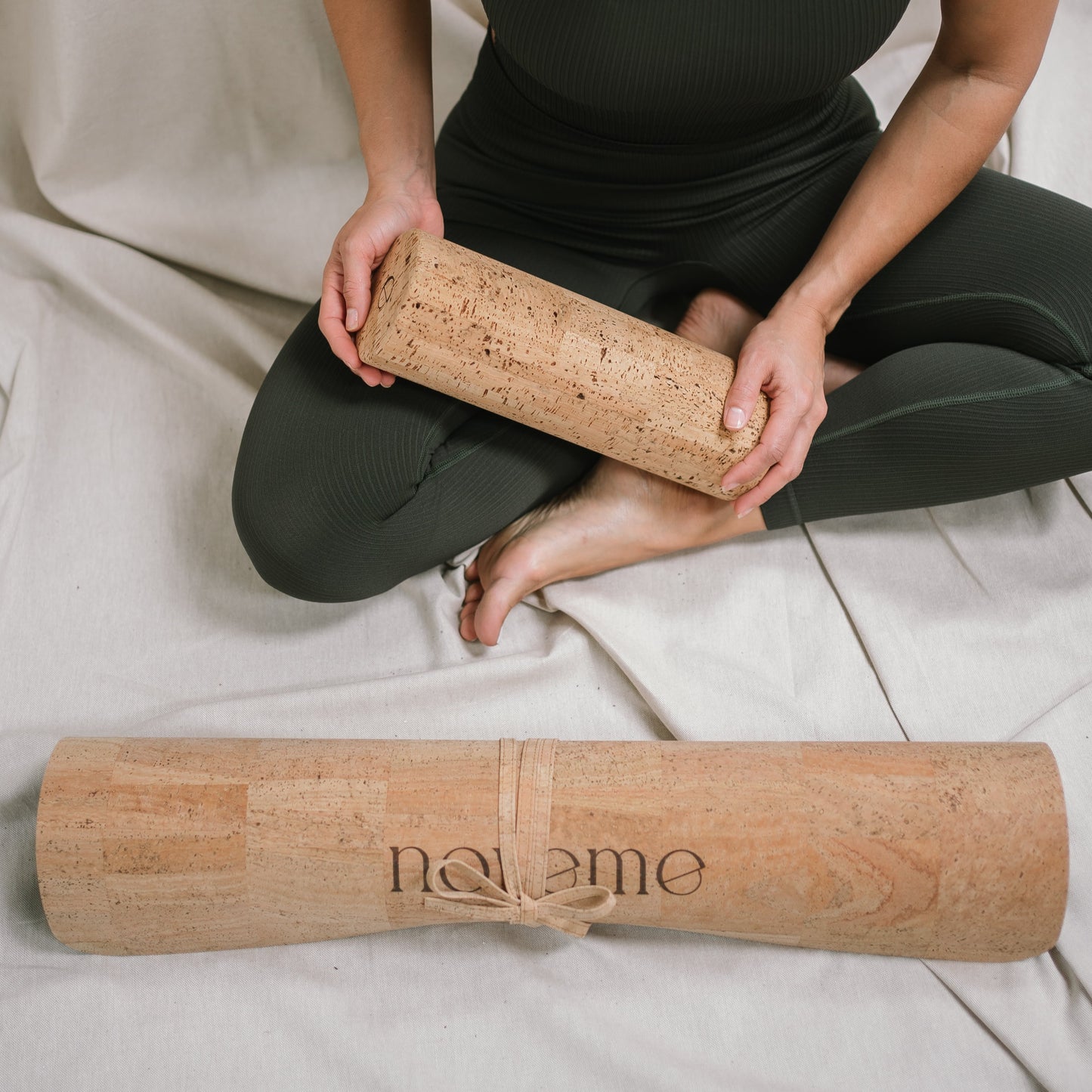 Woman holding a Noveme Cork Roller while seated next to a rolled Noveme Cork Yoga Mat