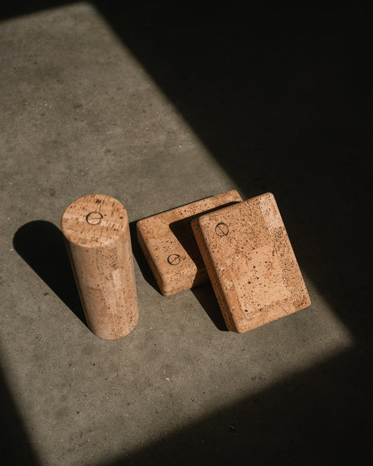 noveme cork yoga accessories, a cork roller and two cork yoga blocks, placed on a concrete floor 