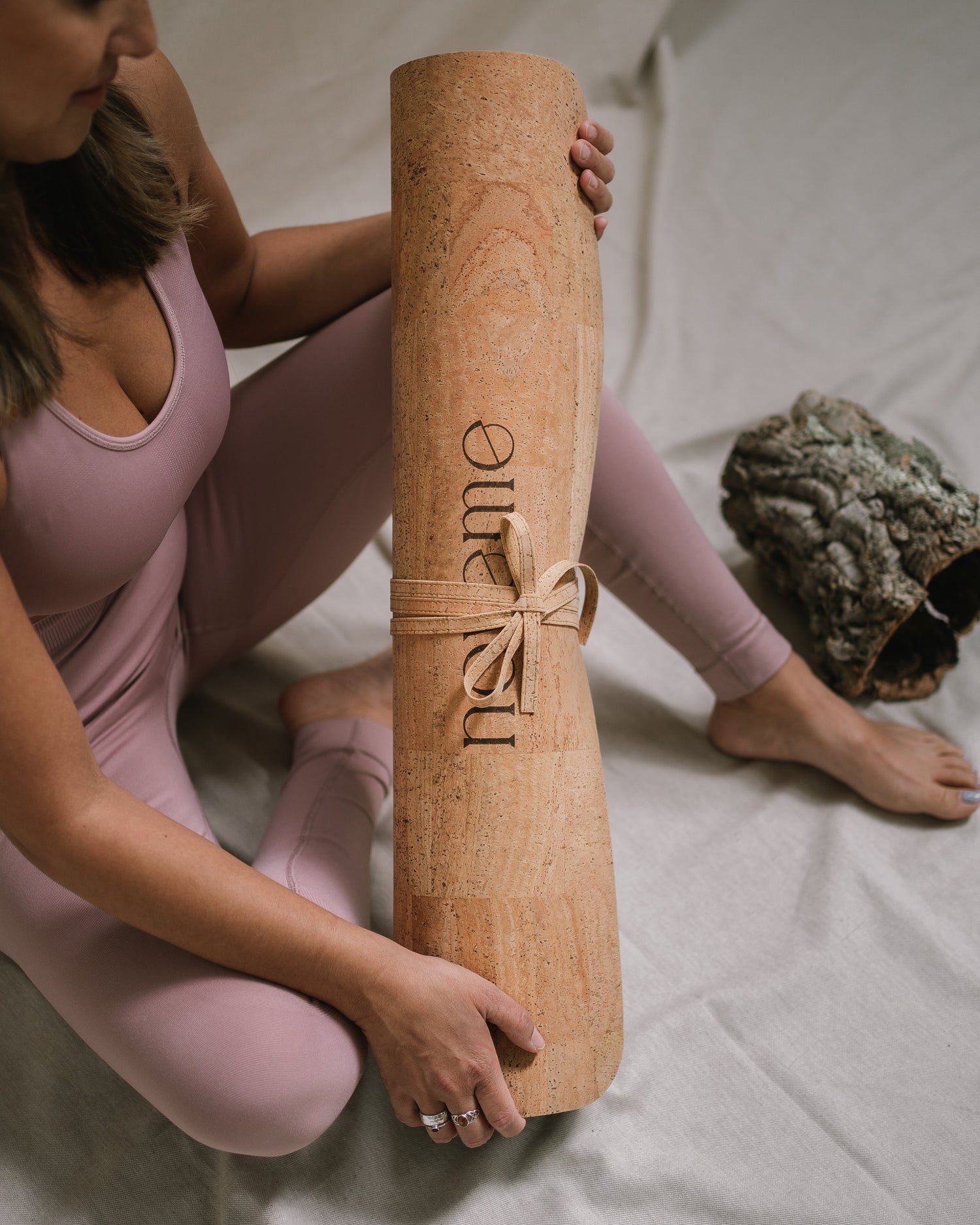 Woman holding a Noveme cork yoga mat while seated next to a piece of cork bark