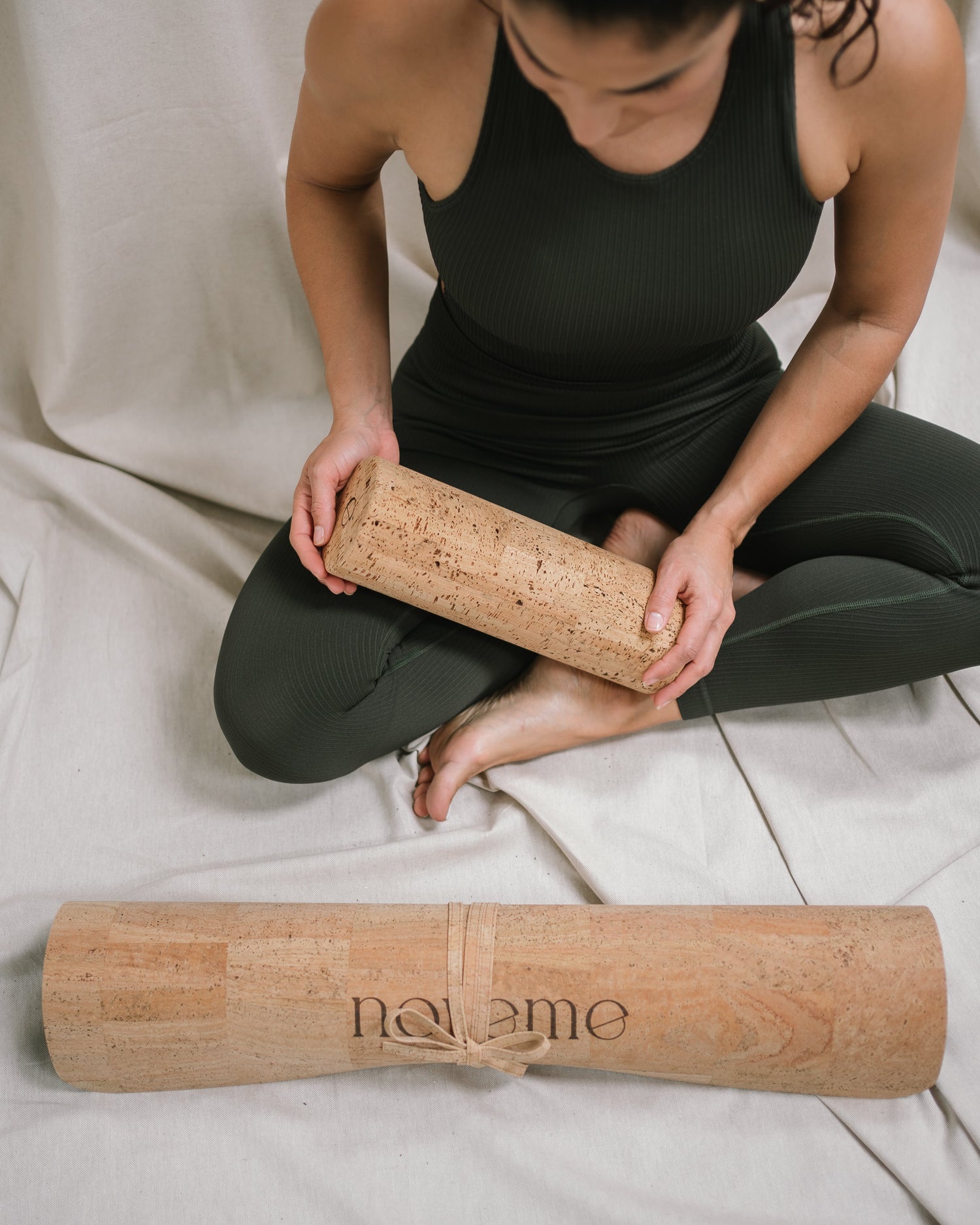 Yogi holding a Noveme cork roller sitting next to a Noveme cork yoga mat