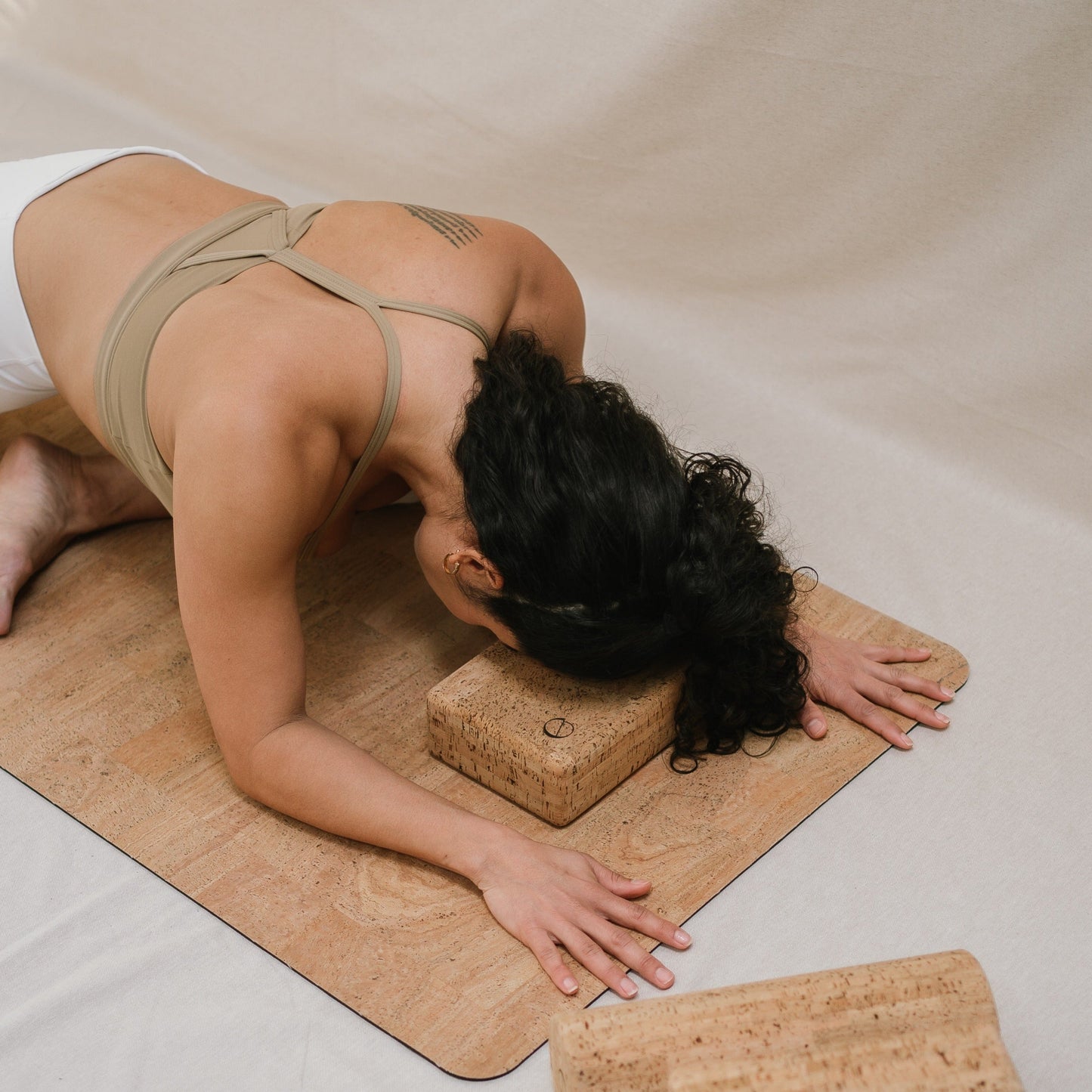 model doing pigeon pose laying her head on a noveme cork yoga block 